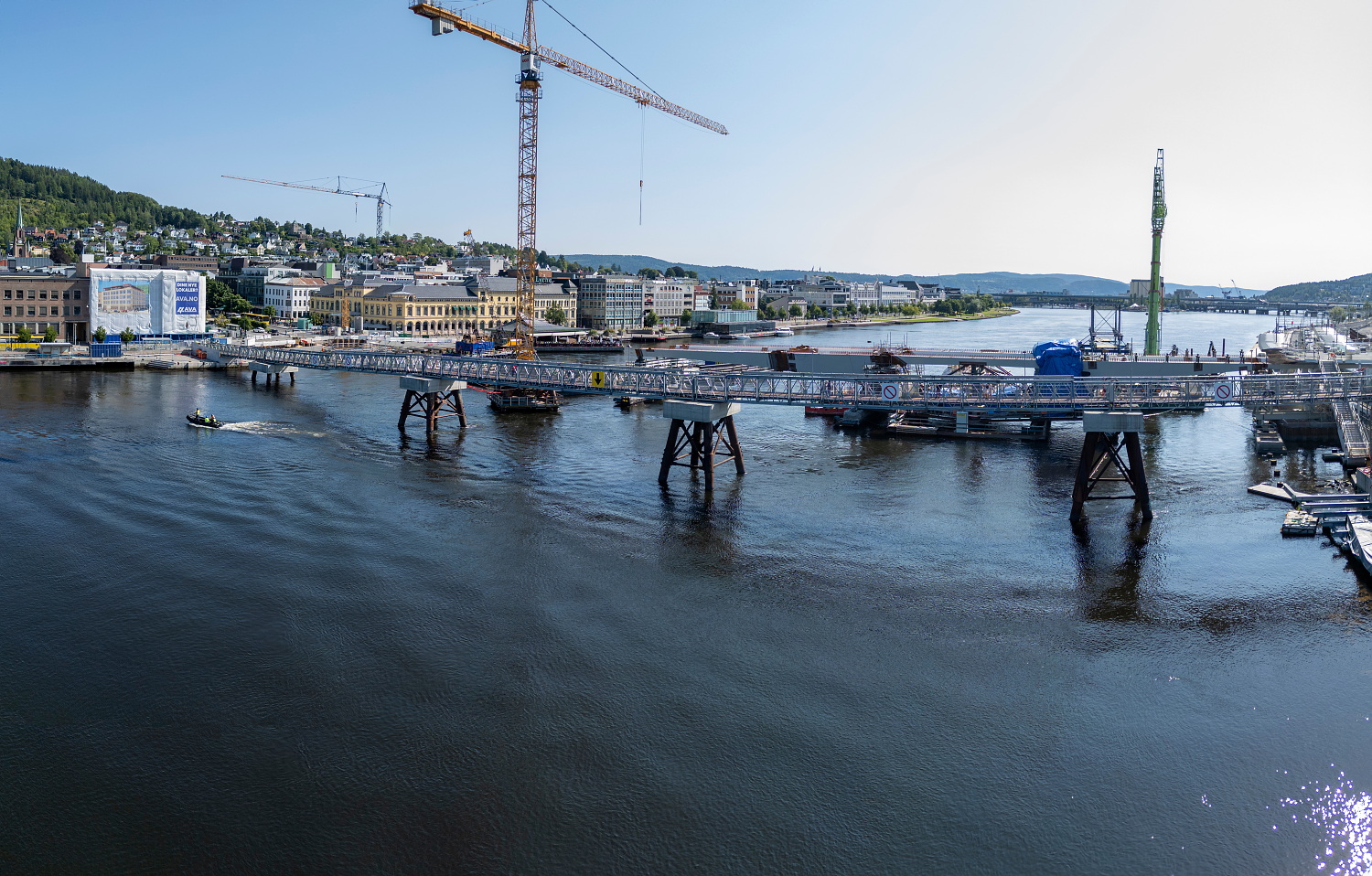 En midlertidig bru over en elv, med en høy kran og anleggsarbeider på baksiden.