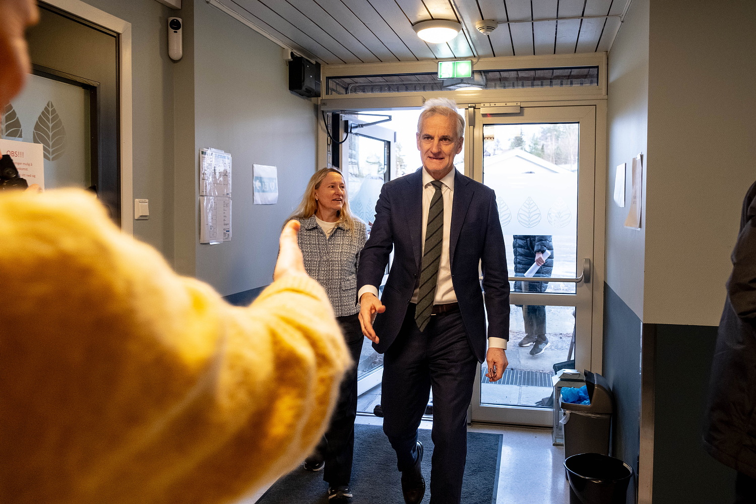 En mann kommer gående med utstrakt hånd for å hilse på en dame som strekker ut hånda. Mannen ser vi forfra, damen ser vi bakfra.