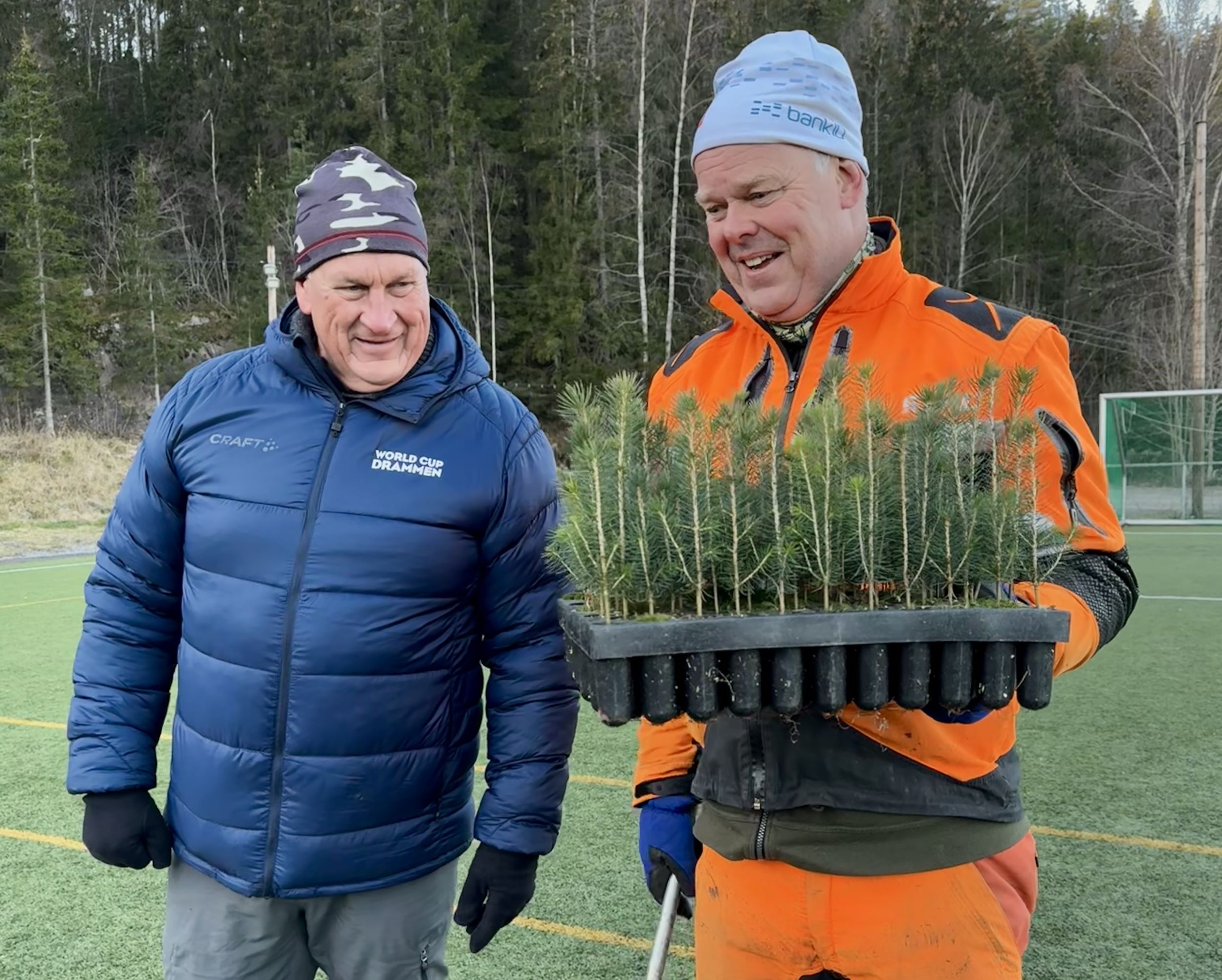 to voksne menn, hvorav en i oransje arbeidstøy, holder et stort brett med granskudd