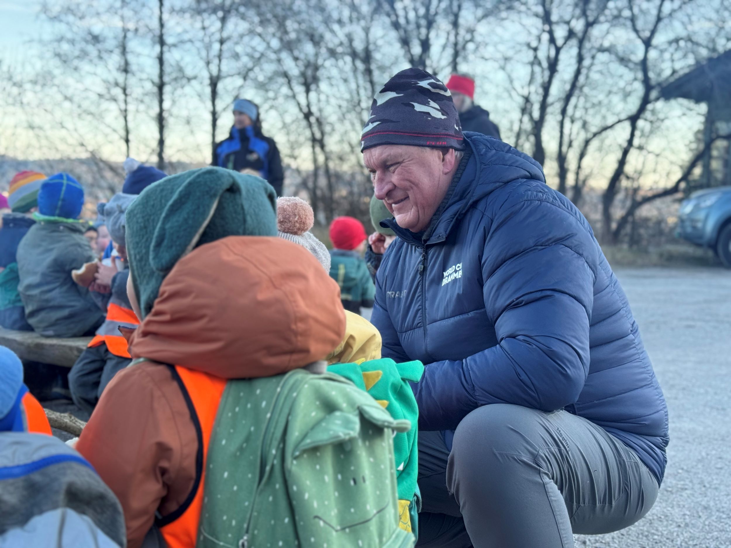 En mann sitter på hun og prater med barn rundt et bål