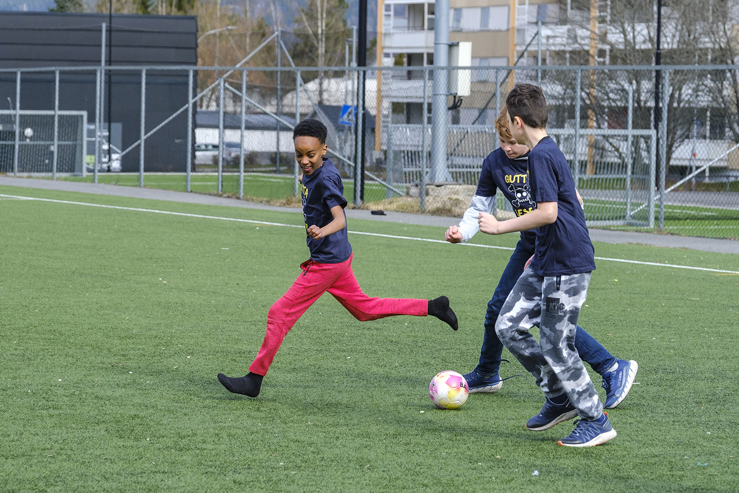 Tre gutter som spiller fotball på kunstgress.